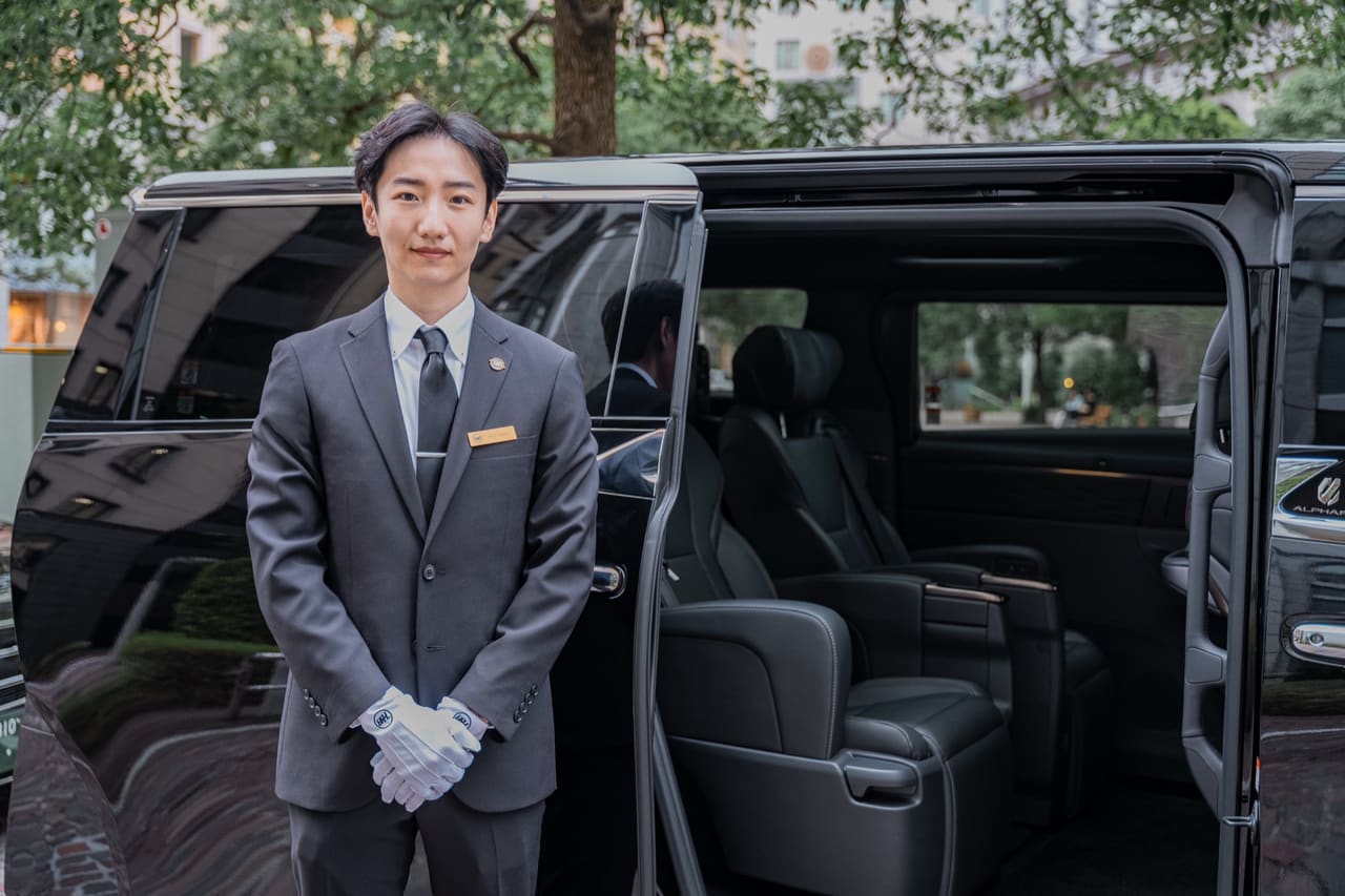 RydAgent chauffeur in a suit and white gloves beside a black Toyota Alphard with the door open